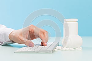 Doctor`s hands in a white medical coat are typing on the keyboard, two white cans with pills and a red heart on a blue background