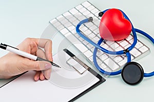 Doctor`s hands in a white medical coat write a prescription, white keyboard and red heart on a blue background. concept of