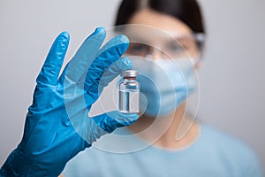 Doctor scientis in protective gloves and mask holding glass vial with injection liquid. Vaccination against influenza and