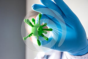 Doctor or scientist hold in hand in medical glove three-dimensional model of virus - coronavirus COVID-19 in foreground of photo c