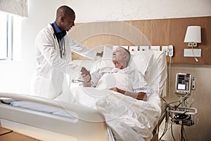 Doctor Shaking Hands With Senior Male Patient In Hospital Bed In Geriatric Unit