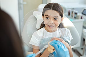 Doctor showing how to brushing teeth on jaws model to girl sitting in dental chair