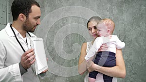 Doctor showing medical results on a tablet to mother and baby boy. White Display.