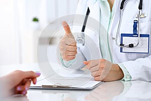 Doctor showing Ok sign and thumb up to patient while sitting at the desk in hospital office, closeup of human hand