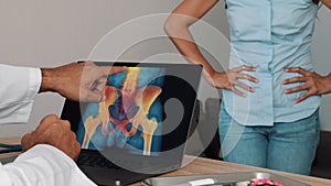 Doctor showing x-ray of pain in the hips on a laptop with woman patient