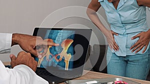 Doctor showing x-ray of pain in the hips on a laptop with woman patient