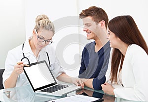 Doctor showing report to couple on laptop