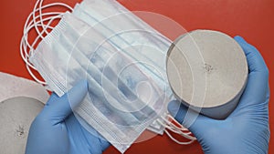 Doctor showing rolls toilet paper and antiviral face masks on red background. Human hands protected blue medical gloves