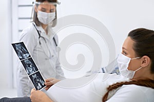 Doctor showing to pregnant woman ultrasound scan of baby