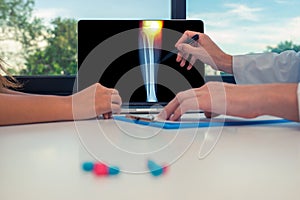 Doctor showing a x-ray of legs with pain in the internal knee on a laptop to a woman patient. Pills on the desk