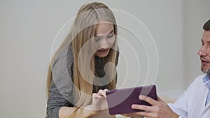 The doctor shows a picture of an ultrasound on a tablet to a pregnant woman. A happy future mother admires a picture of