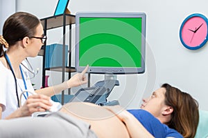 A doctor shows a pregnant patient her unborn baby on an ultrasound screen. Green screen. Gynecology office.