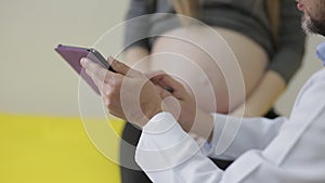 The doctor shows the pregnant woman on the tablet the problem of her pregnancy. Close-up