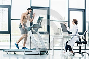 doctor sitting at computer desk and conducting endurance test with sportsman in gym.