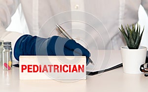 a doctor sitting in a desk with a injured teddy bear and a nameplate with the word paediatrician written in it
