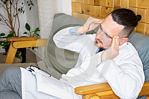 A doctor sitting in his cabinet after a hard working day, tired but still reading something and working to make his patients healt