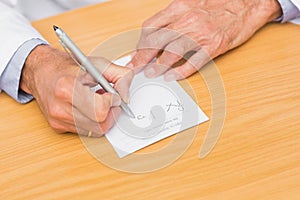 Doctor sitting at his desk writing on prescription pad