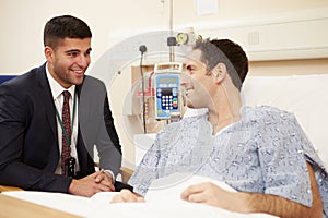 Doctor Sitting By Male Patient's Bed In Hospital