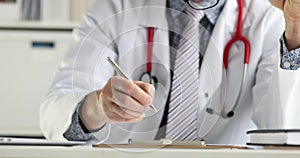 Doctor sitting at table and filling out medical history with pen 4k movie