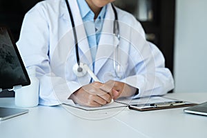 Doctor sitting at table and writing on a document report in hospital office. Medical healthcare staff and doctor service