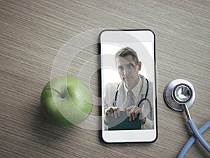 Doctor on smartphone screen, stethoscope and green apple on table, doctor online concept, online medical communication and medical