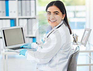 Doctor, smile and working on laptop mockup with medical healthcare employee at her desk in hospital consulting room or