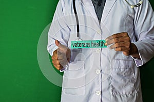 A doctor standing, Hold the Veterans Health paper text on Green background. Medical and healthcare concept photo