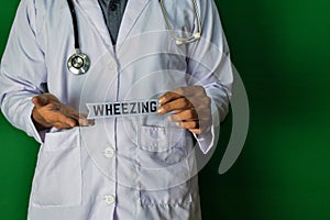 A doctor standing, Hold the Wheezing paper text on Green background. Medical and healthcare concept