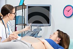 A lady doctor shows a pregnant patient her unborn baby on the ultrasound screen. Gynecology office.