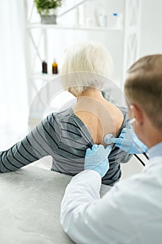 Doctor in sterile gloves examining old woman with stethoscope