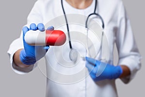 A doctor with a stethoscope, close-up holding a white red capsule