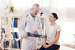 Doctor with stethoscope and female patient in office. Doctor is showing x-ray of hips.