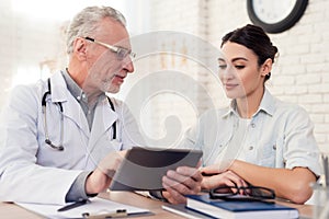 Doctor with stethoscope and female patient in office. Doctor is using tablet.