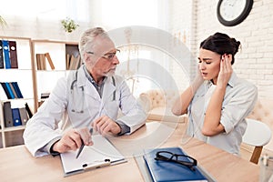 Doctor with stethoscope and female patient in office. Patient`s head hurts.