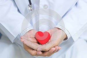 Doctor with stethoscope hand holding red heart shape in the hospital