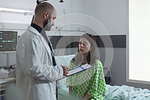 Doctor with stethoscope holding clipboard with patient medical history discussing treatment with woman sitting