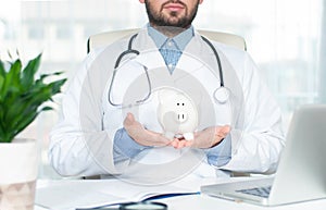 Doctor with stethoscope holding piggy bank.