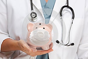 Doctor with Stethoscope Holding Piggy Bank Wearing Medical Face Mask