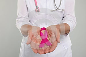 Doctor with stethoscope holding pink ribbon on light grey background, closeup. Breast cancer awareness