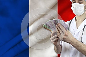 Doctor with a stethoscope holds euro banknotes in the background of the silk national flag of France, the concept of medical