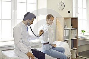 Doctor with stethoscope listening to woman& x27;s back to examine her breath or heartbeat