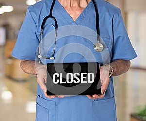 Doctor with stethoscope in medical scrubs holding electronic tablet saying hospital is closed