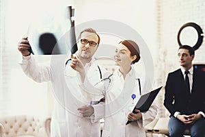 Doctor with stethoscope and nurse examines X-ray of businessman, of patient.