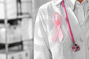 Doctor with stethoscope and pink ribbon indoors, closeup and space for text. Breast cancer awareness