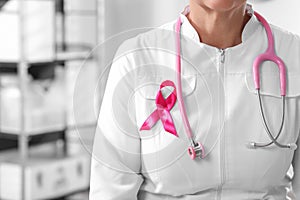 Doctor with stethoscope and pink ribbon indoors, closeup and space for text. Breast cancer awareness