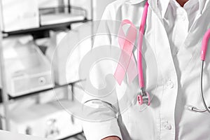 Doctor with stethoscope and pink ribbon indoors, closeup and space for text. Breast cancer awareness