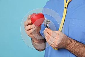 Doctor with stethoscope and red heart on light blue background, closeup. Cardiology concept