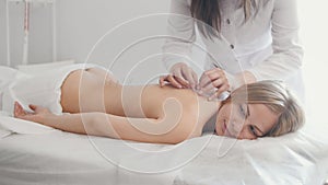 The doctor sticks needles into the woman`s body on the acupuncture