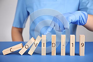 Doctor stopping domino effect at blue table, closeup. Prevent spreading of coronavirus