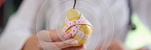 Nutritionist showing ripe yellow pear with measuring tape while sitting in medical office.